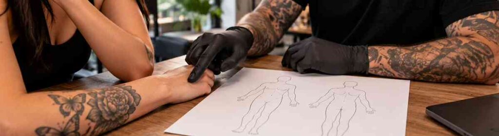 Tattoo artist discussing tattoo placement with a client using body sketches