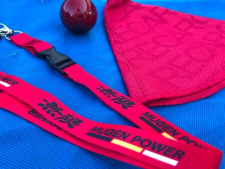 Red Mugen Power lanyard and bride shift boot fabric close-up on blue surface.