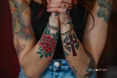 Christian Tattoos: Person with arms crossed showcasing detailed Christian-themed tattoos, including a red rose and a cross.