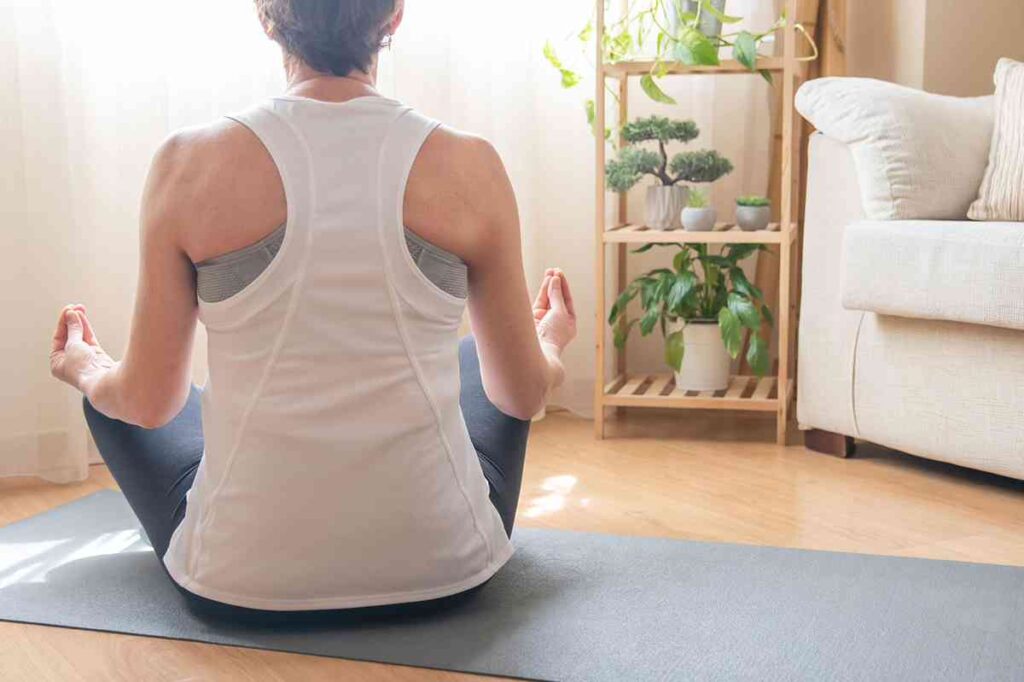 Woman in comfortable workout clothes practicing seated meditation on a yoga mat at home