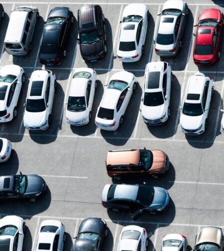 A crowded parking lot from above with one car pulling out of a spot while five others hover, waiting to pull in.