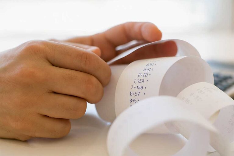 Close-up of hands holding a curled receipt tape with printed calculations, under soft natural light.