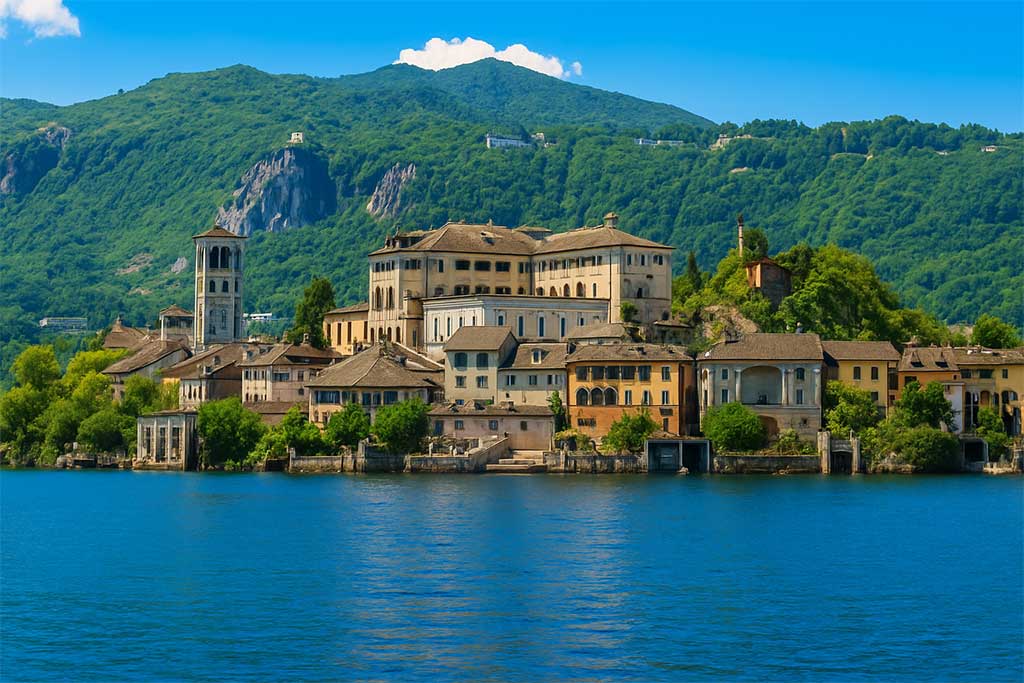 Historic buildings of Orta San Giulio by the calm waters of Lake Orta with green hills in the background.