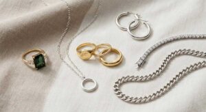 Fine jewelry flat lay with gold rings, silver necklace, hoop earrings, and gemstone pieces on a neutral luxury background