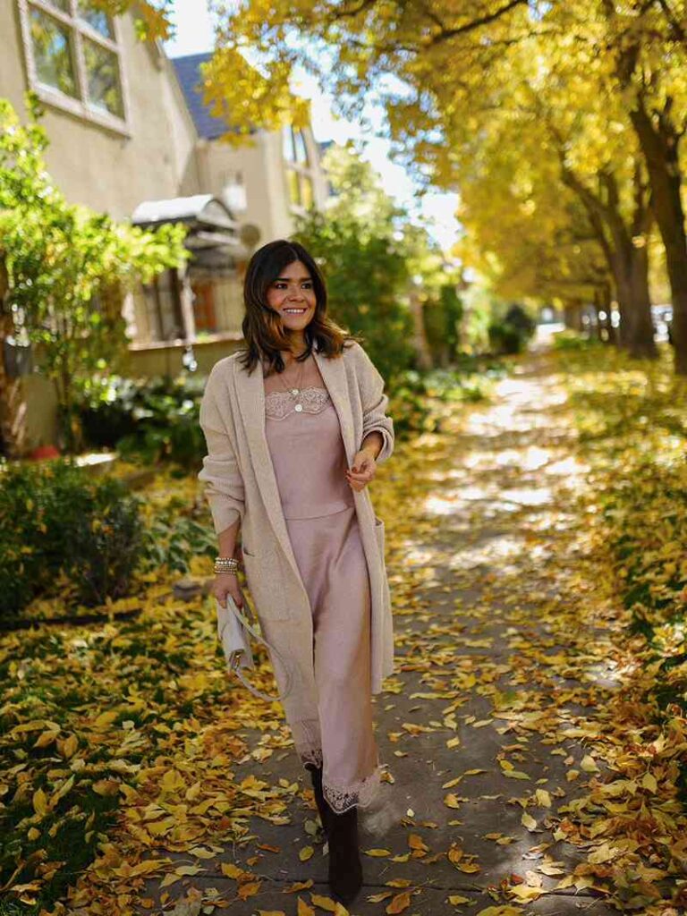 Carolina Hellal wearing a pink dress, beige cardigan, and dark boots on an autumn walkway