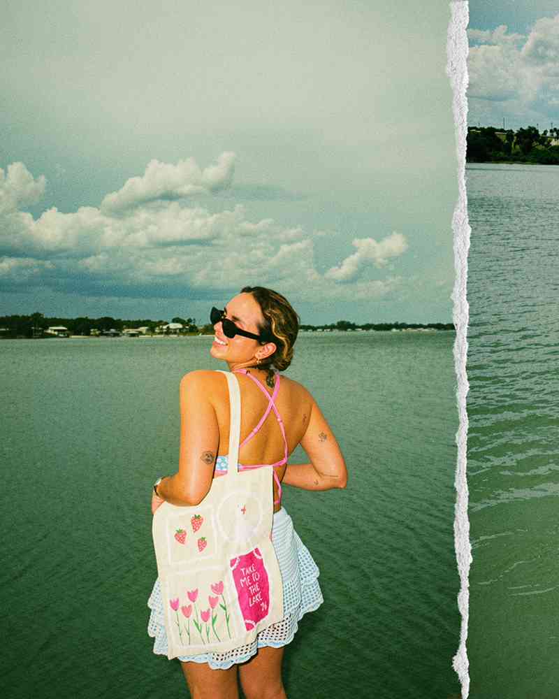 Daniela Ramirez wearing a pink strappy top, blue ruffled skirt, and sunglasses by a lake