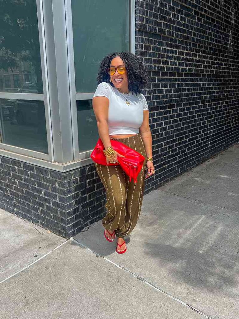 Jennifer of Jenswear wearing a white cropped top, printed trousers, and red sandals with a red clutch